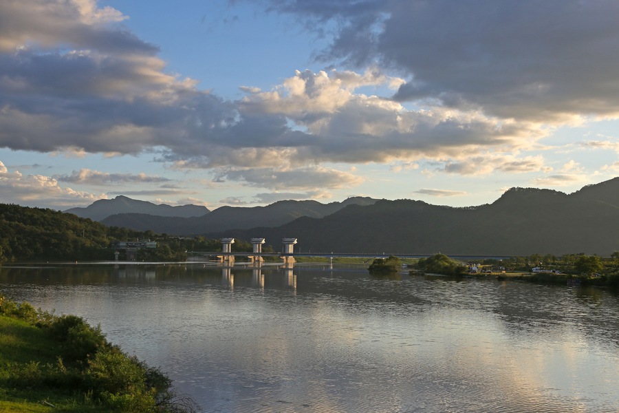 A calm lake with mountains in the background and a bridge with three pillars in the foreground.