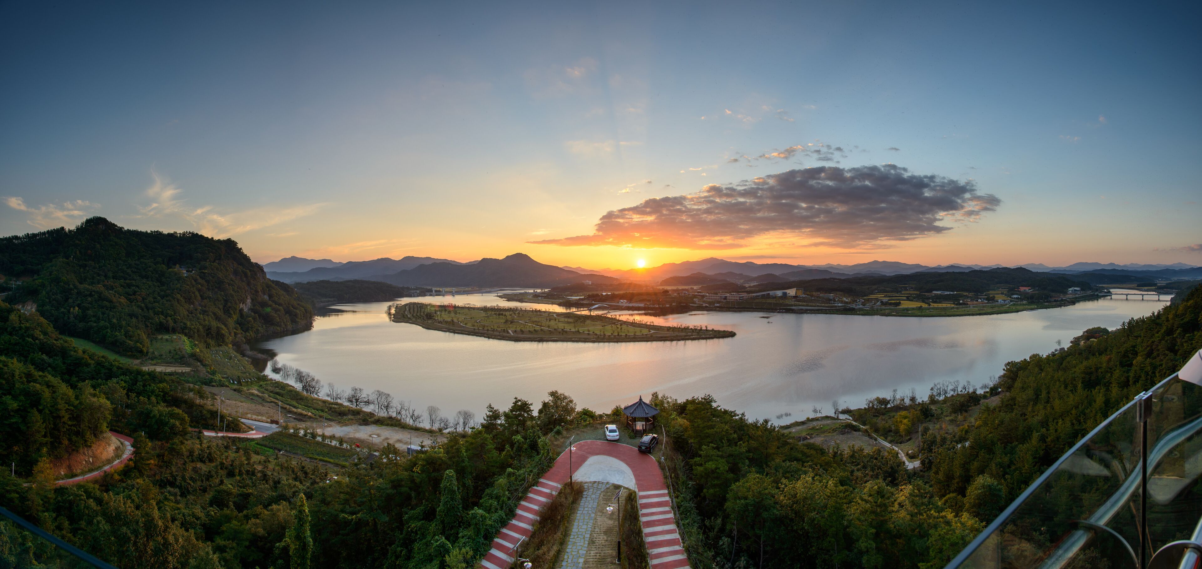 A scenic landscape with a lake, mountains, and a sunset.