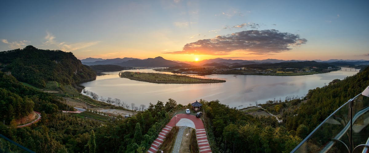 A scenic landscape with a lake, mountains, and a sunset.