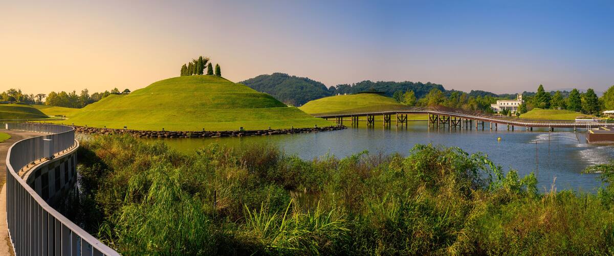 A bridge over a lake, surrounded by green hills and trees.