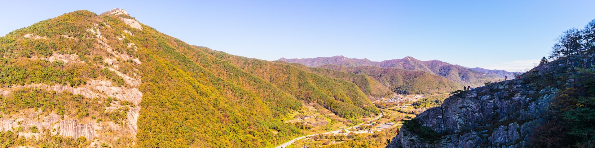 Un paisaje montañoso con una carretera sinuosa, bosques densos y riscos rocosos.