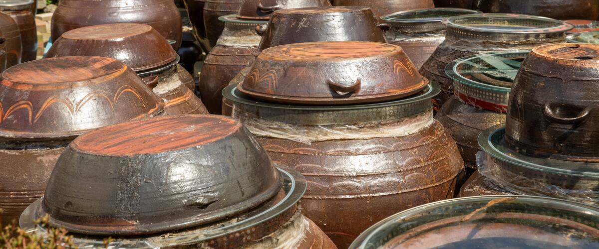 A collection of large, rustic pottery jars with lids, arranged outdoors.