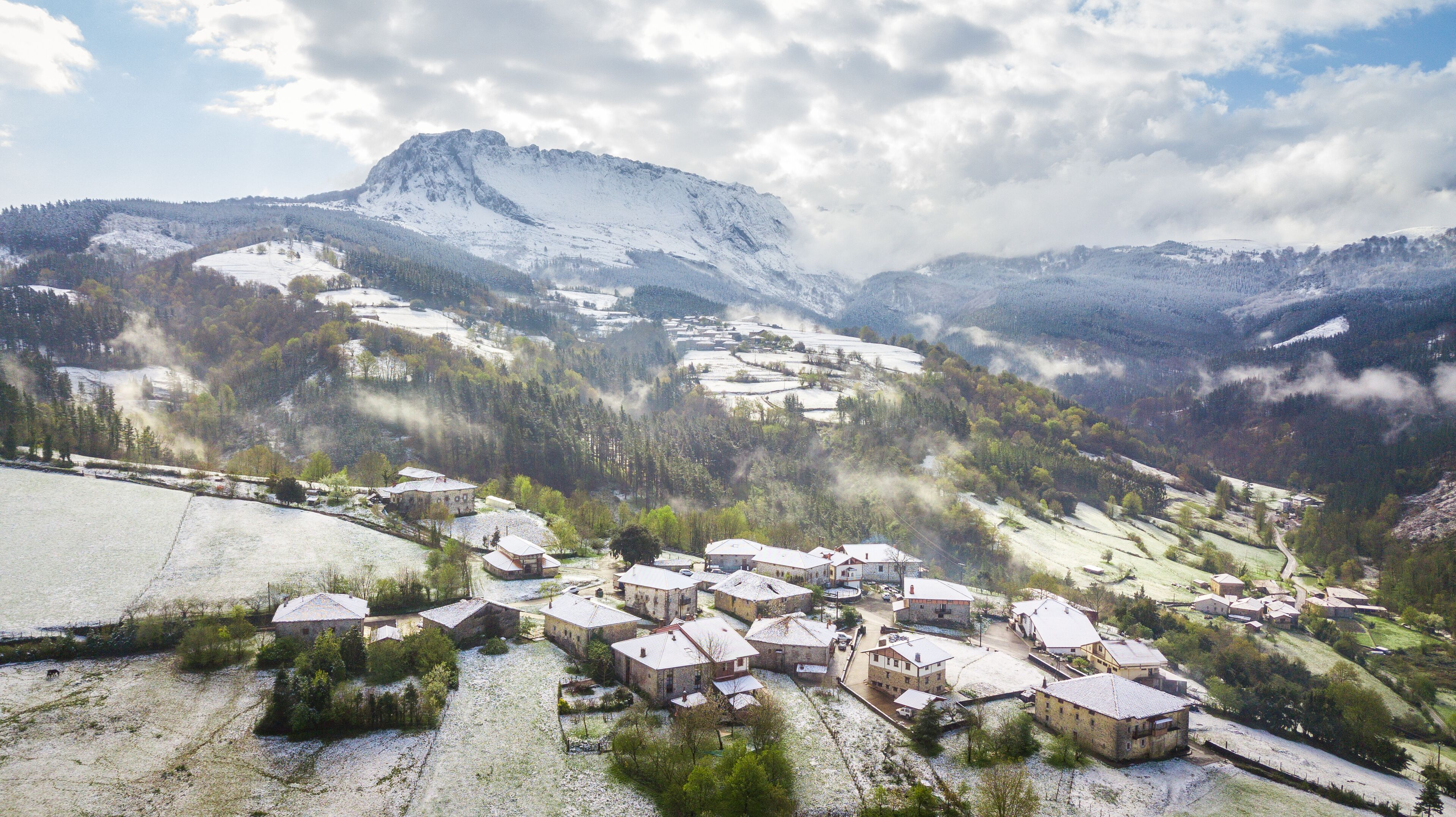A snow-covered village with traditional houses, surrounded by mountains and forests.