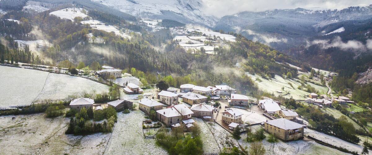 A snow-covered village with traditional houses, surrounded by mountains and forests.