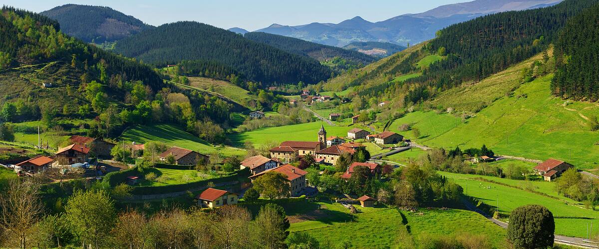 A picturesque village nestled in a valley surrounded by lush green hills and mountains.