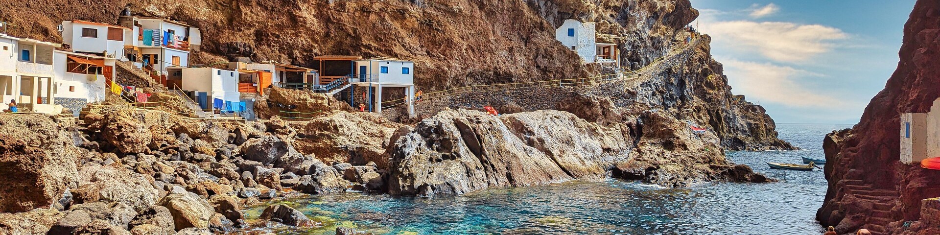 A coastal village with white buildings, rocky cliffs, and clear blue waters.
