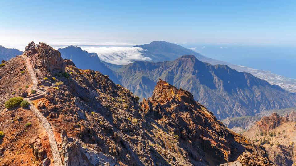A rugged mountain landscape with a clear sky and a distant view of the coastline.
