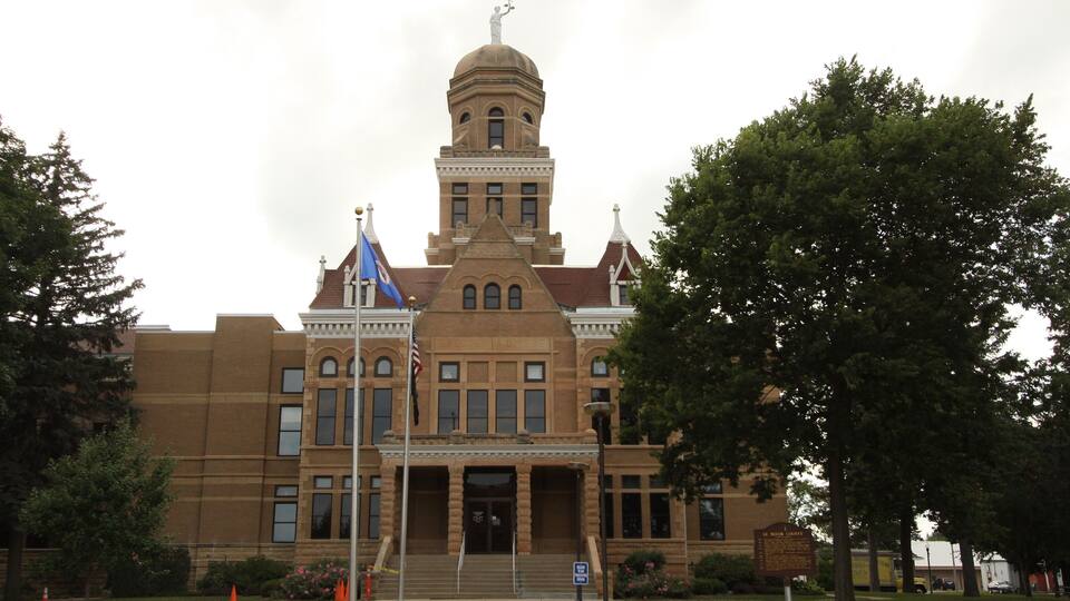 A large brick building with a central dome and a flagpole with flags.
