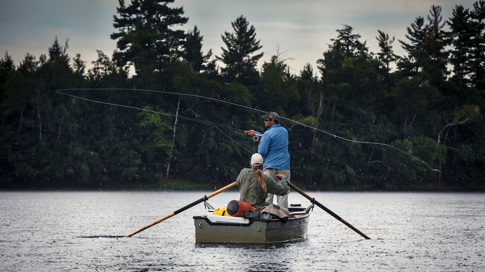 A small boat on a lake with two people fishing.