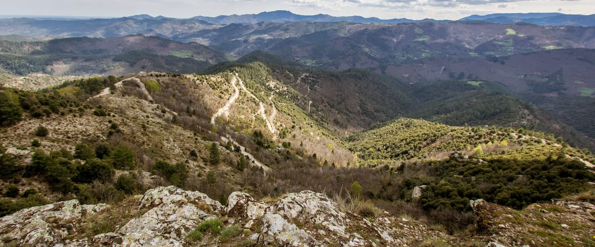 A mountainous landscape with a winding path, rocky terrain, and dense forests.