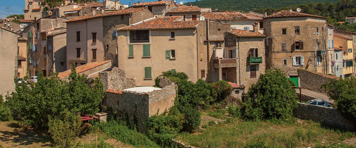 A historic village with terracotta-roofed buildings, lush greenery, and a clear blue sky.