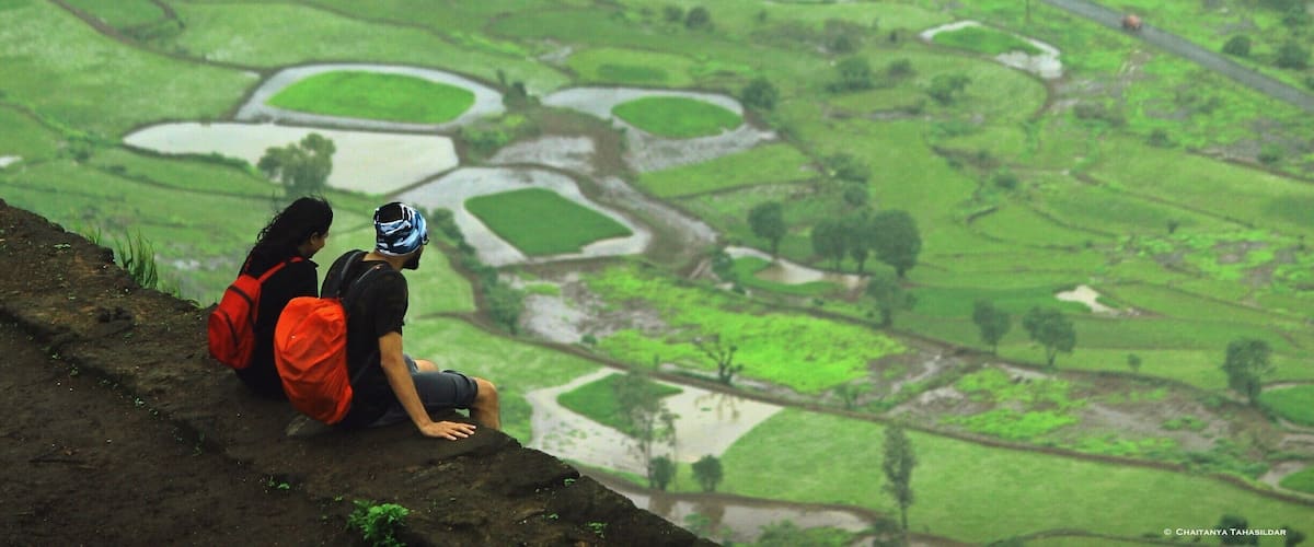 Two people sitting on a hillside overlooking a terraced rice field.