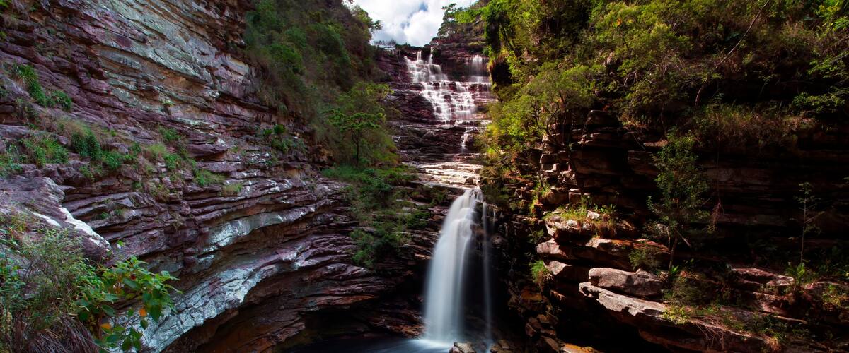 A waterfall cascading down a rocky gorge surrounded by lush greenery.