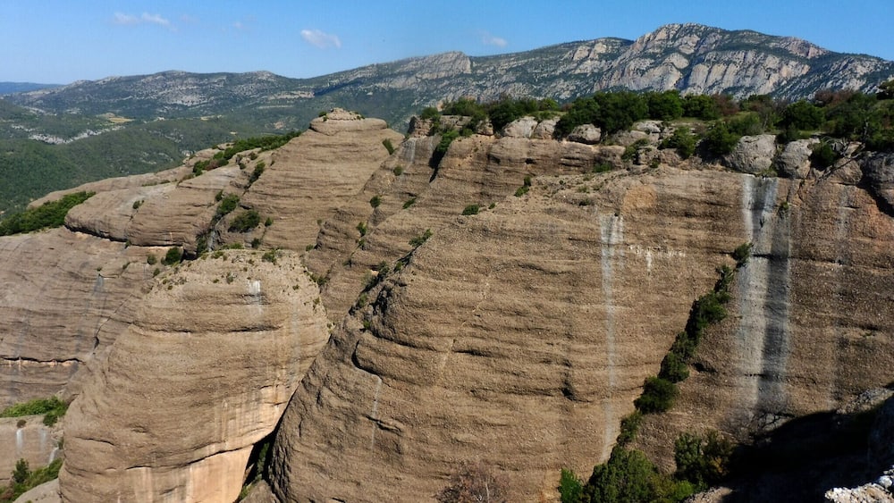A rocky mountain landscape with layered rock formations and a waterfall.