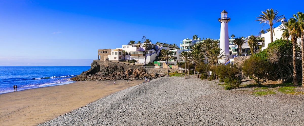 A coastal scene with a beach, a lighthouse, and buildings on a rocky outcrop.