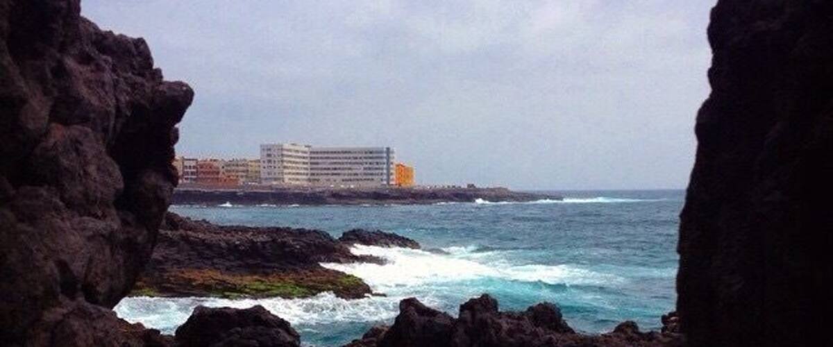 A rocky coastline with waves crashing against the rocks and a building in the background.