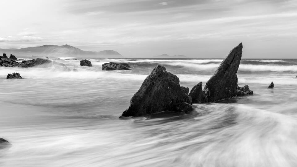 A black and white coastal scene with prominent rock formations and waves.
