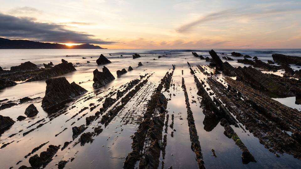 A rocky shoreline with tide pools and a sunset in the background.