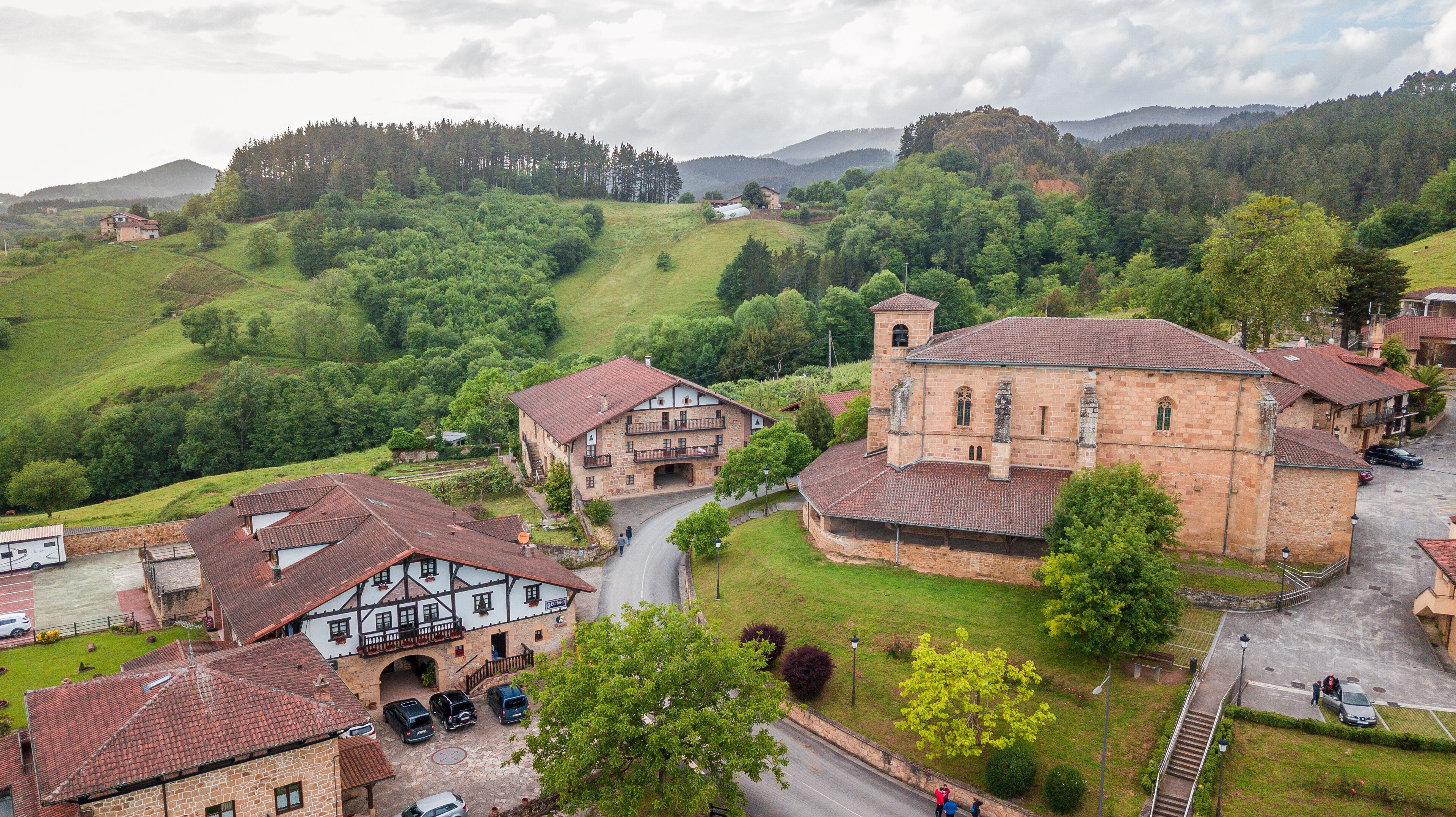 A rural village with traditional stone buildings, a church, and rolling green hills in the background.