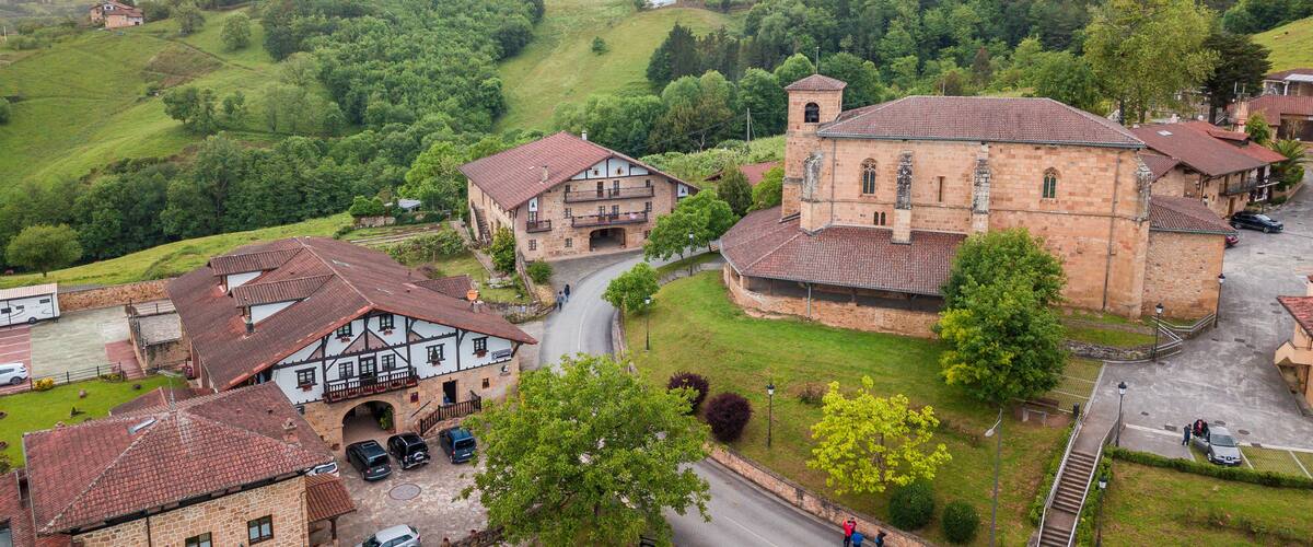 A rural village with traditional stone buildings, a church, and rolling green hills in the background.