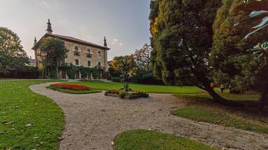 A garden with a gravel path, a fountain, and a large tree.