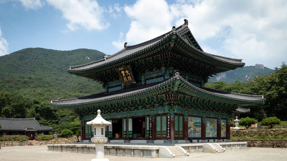 A traditional Korean temple with ornate architecture, surrounded by lush greenery and mountains.