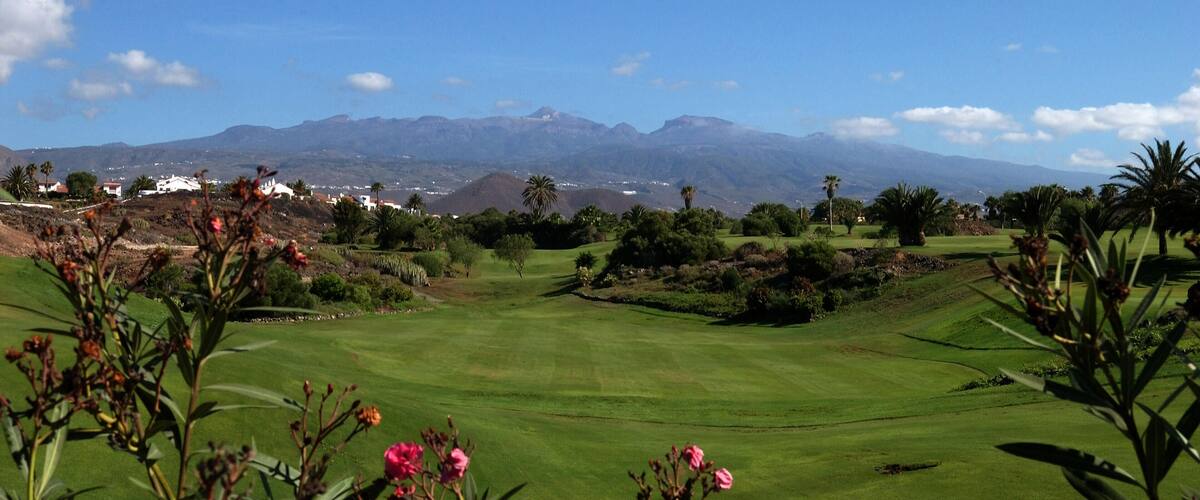 A golf course with a mountainous backdrop and a clear sky.