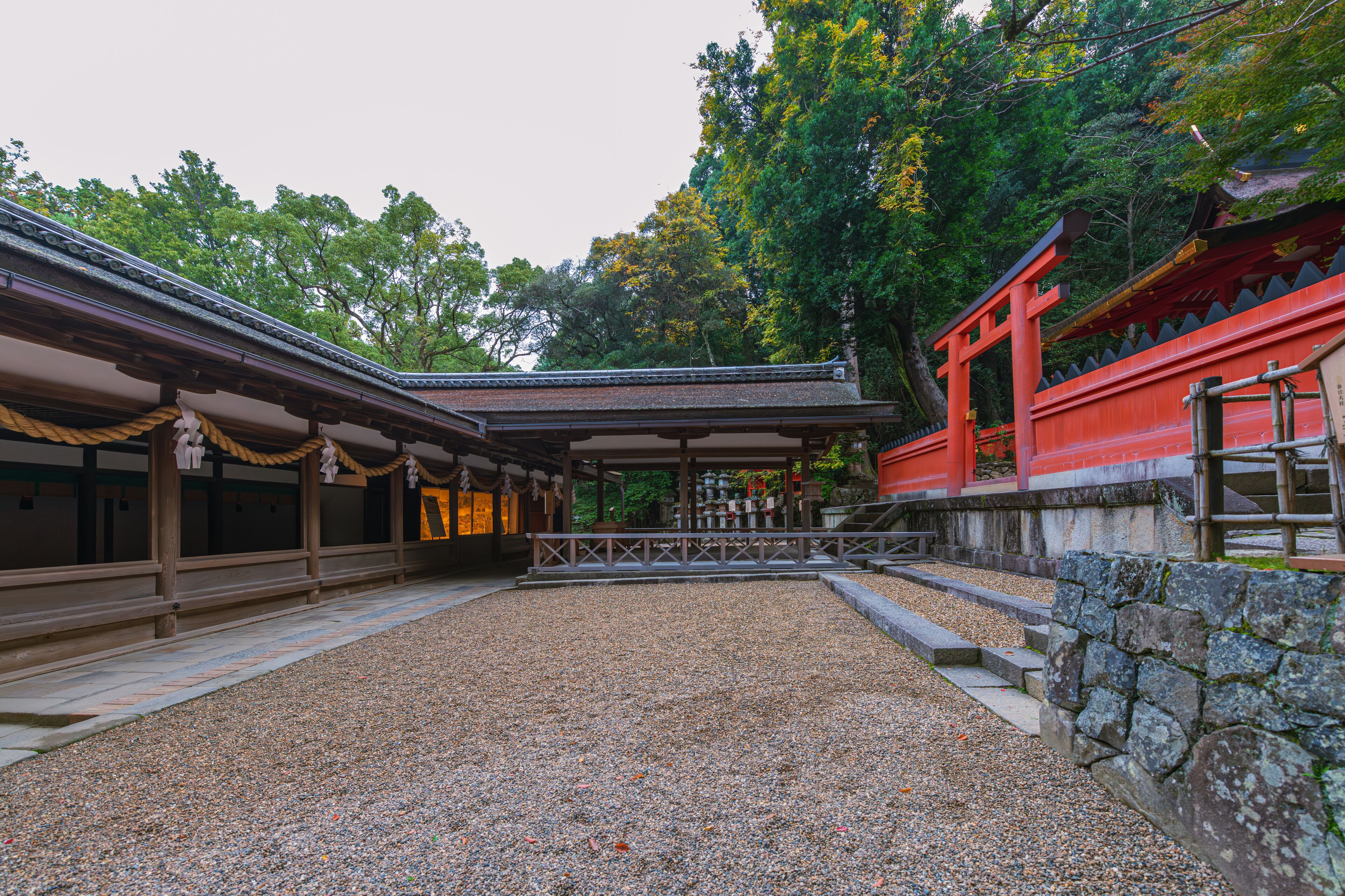 A traditional Japanese temple with a gravel courtyard, wooden structures, and a red torii gate.
