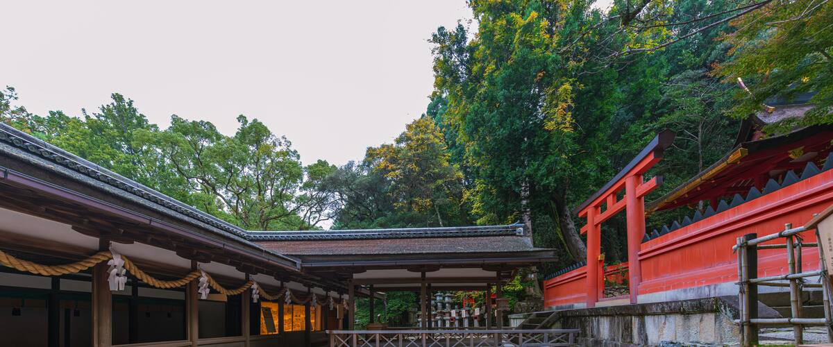 A traditional Japanese temple with a gravel courtyard, wooden structures, and a red torii gate.