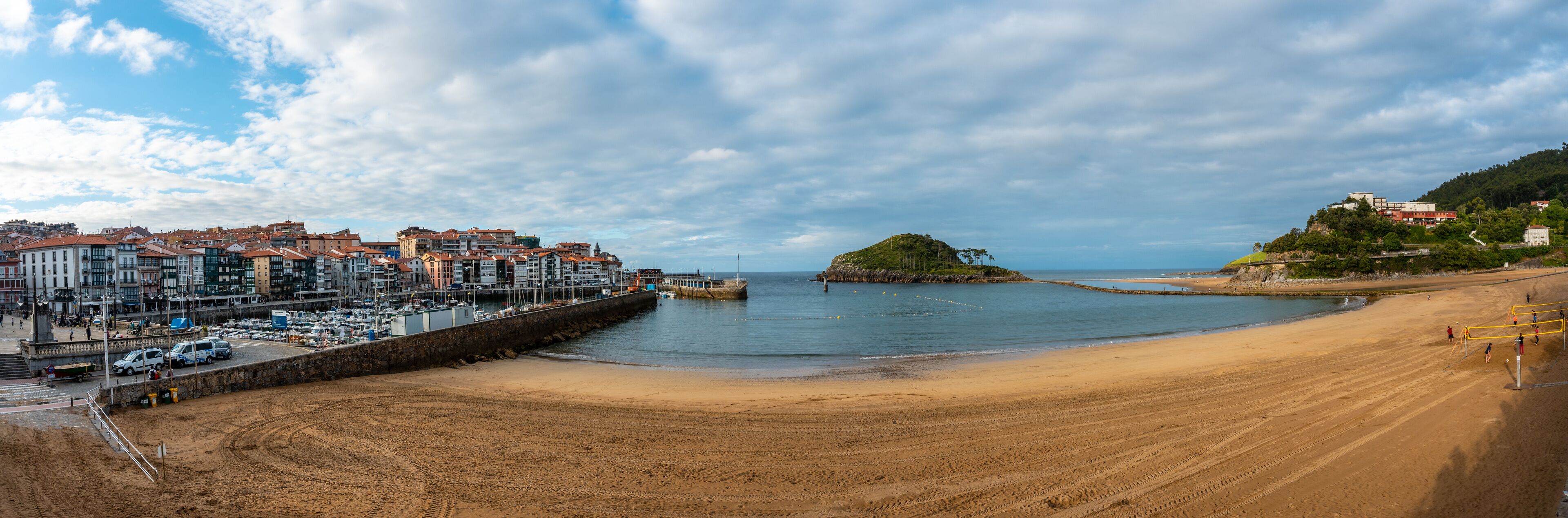 A coastal town with a sandy beach, a rocky island, and a marina with boats.