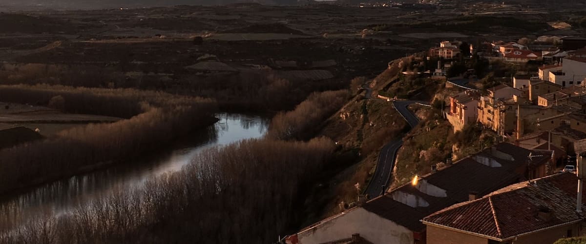 A river winding through a valley with mountains in the background and a town with buildings on a hillside.