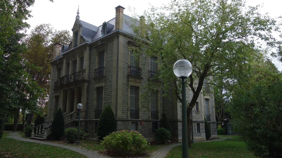 A historic stone building with a grand entrance, a well-maintained garden, and a classic street lamp.
