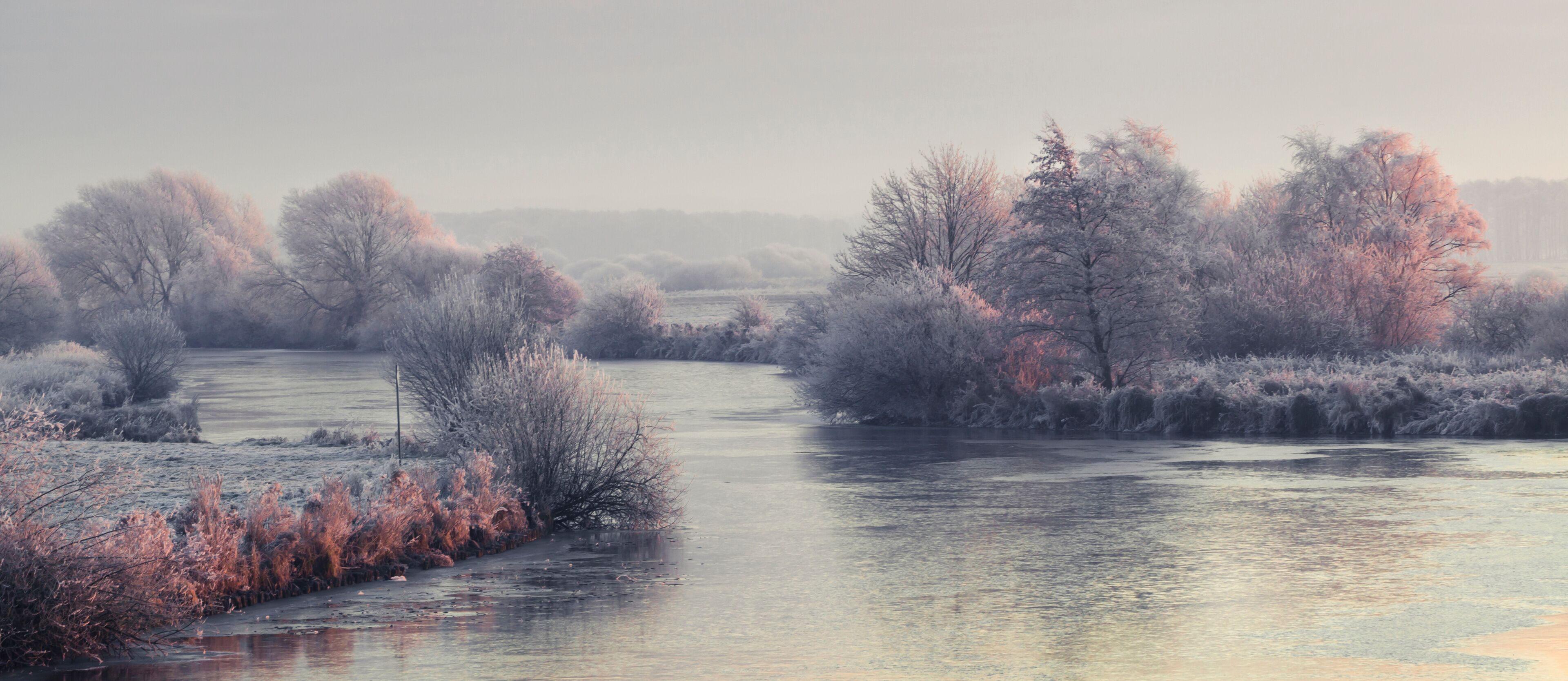 A river surrounded by frost-covered trees and bushes.