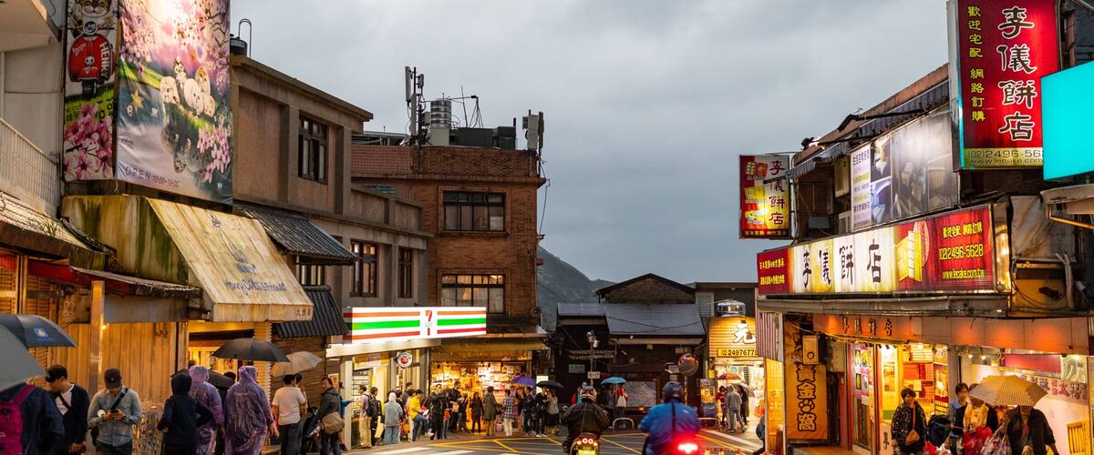 A busy street with shops, a 7-Eleven, and a mountain in the background.