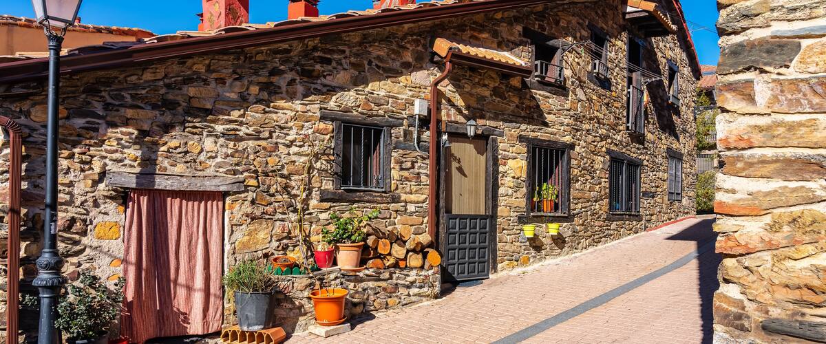 A stone building with a tiled roof, wooden shutters, and potted plants.