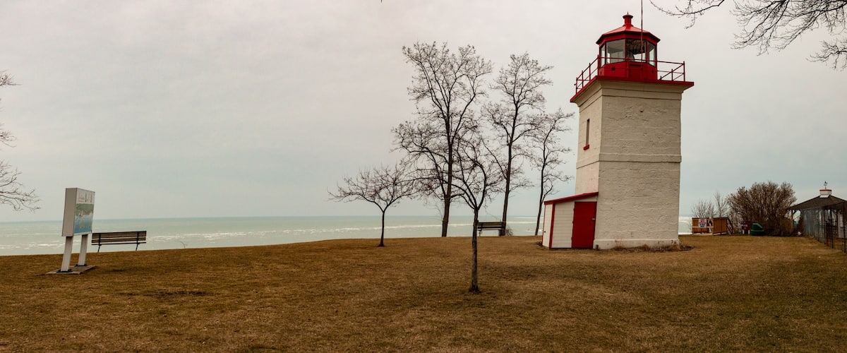 A lighthouse, a bench, and leafless trees by the ocean.