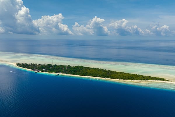 Eine Luftaufnahme einer tropischen Insel mit klarem türkisblauem Wasser, einem Sandstrand und üppiger Vegetation.