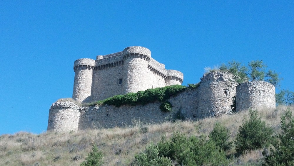 A medieval stone castle with multiple towers and a surrounding grassy hill.