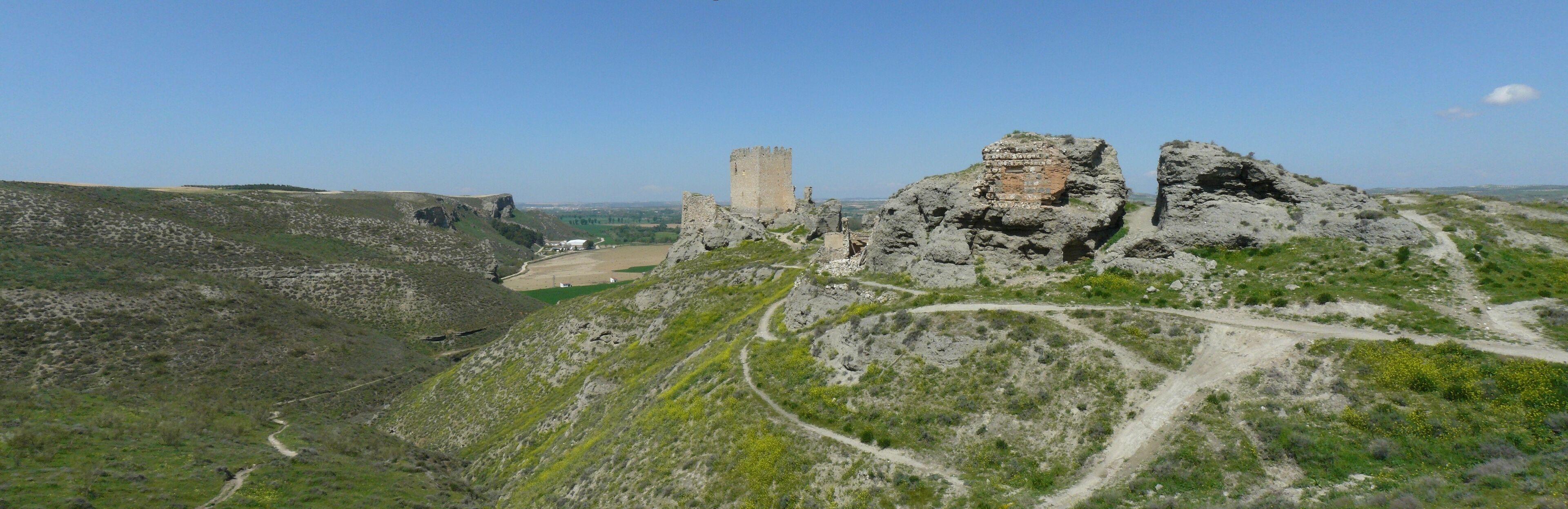 A castle on a hill with a surrounding landscape of rocky terrain and sparse vegetation.