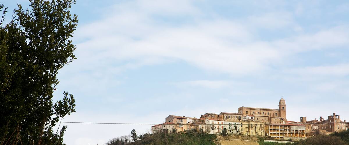 A historic hilltop town with a prominent church and tower, surrounded by hills and trees.