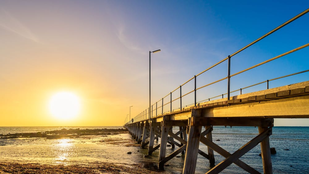 A pier extending into a calm body of water during sunset.