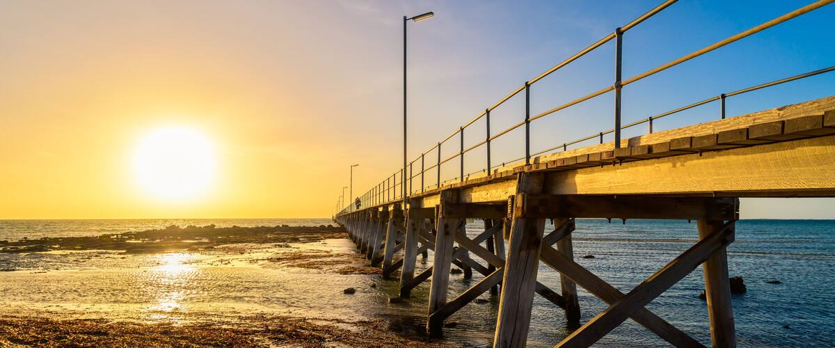 A pier extending into a calm body of water during sunset.