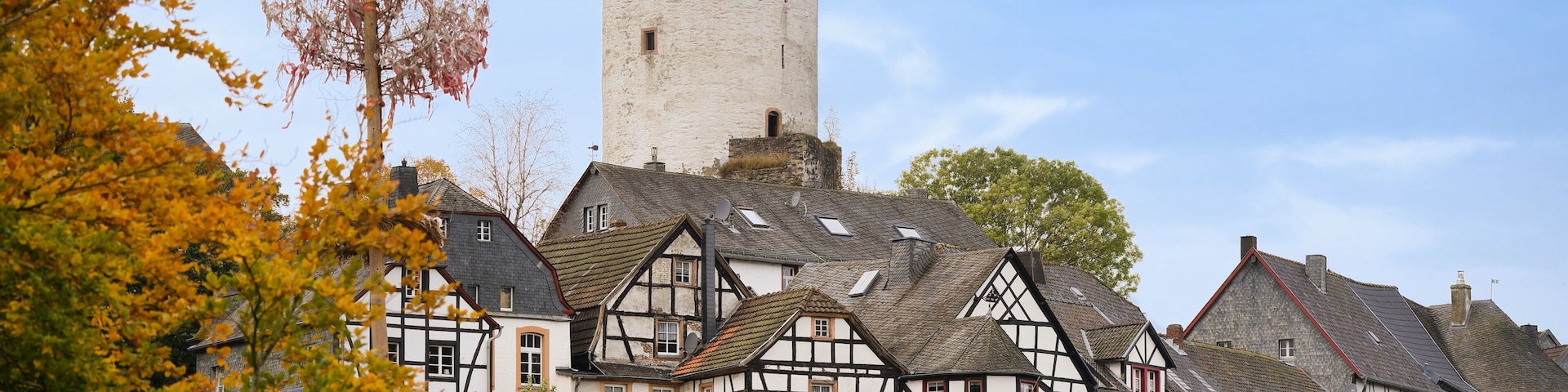 Historic view of Reifferscheid with white castle tower and traditional half-timbered houses. Autumn foliage and clear sky, Eifel region, Germany