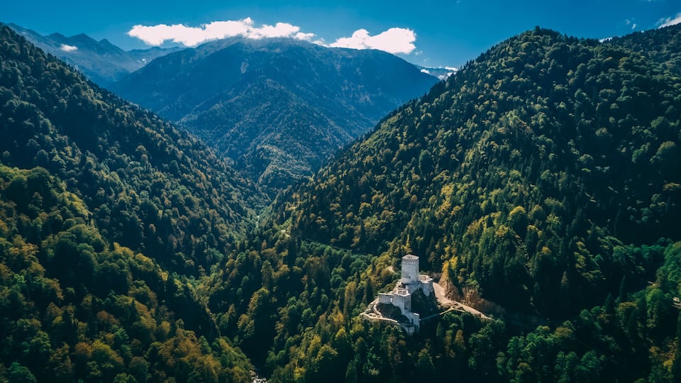 A mountainous landscape with dense forests and a white building with a stone pathway.