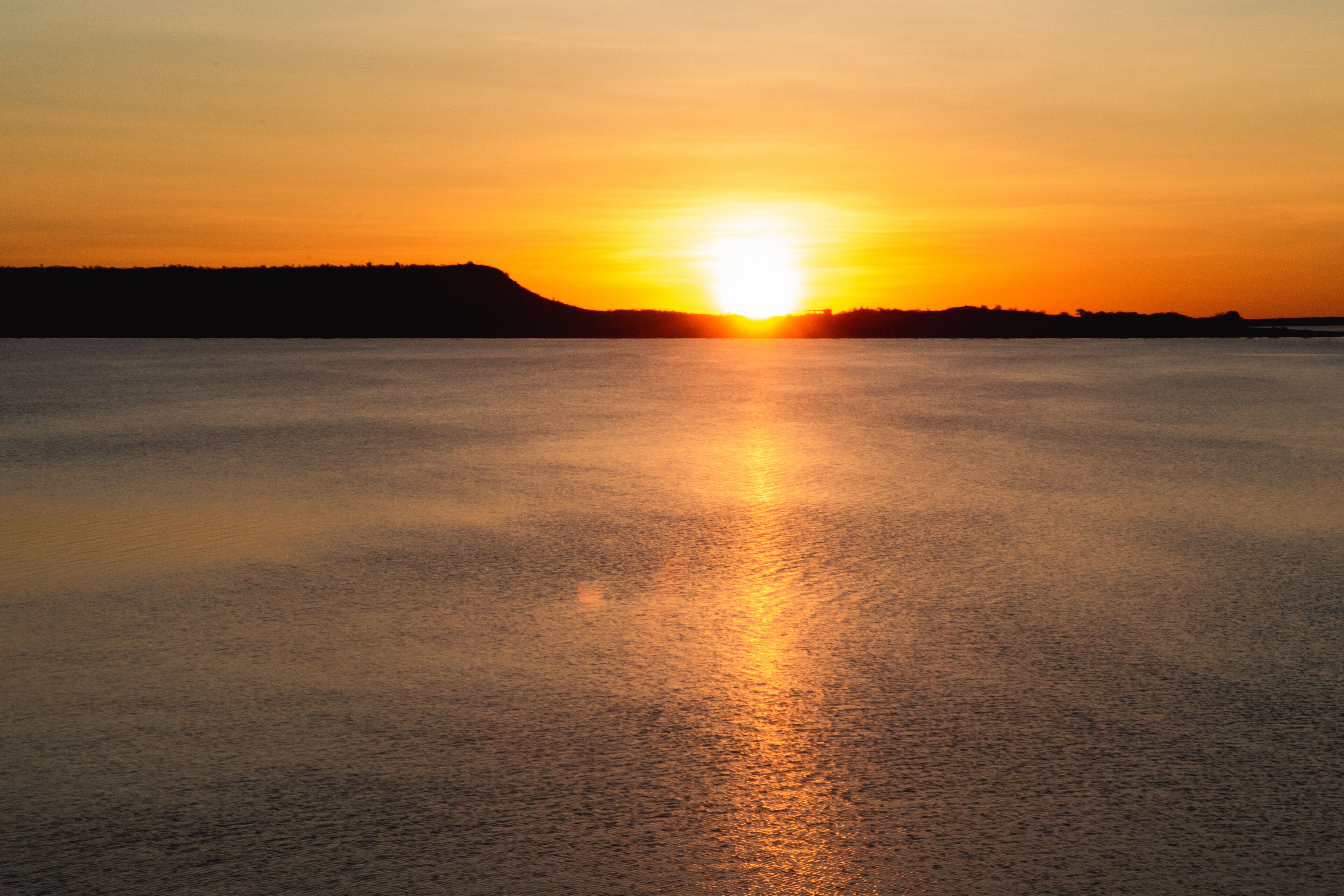 A sunset over a calm body of water with a silhouette of a hill in the background.