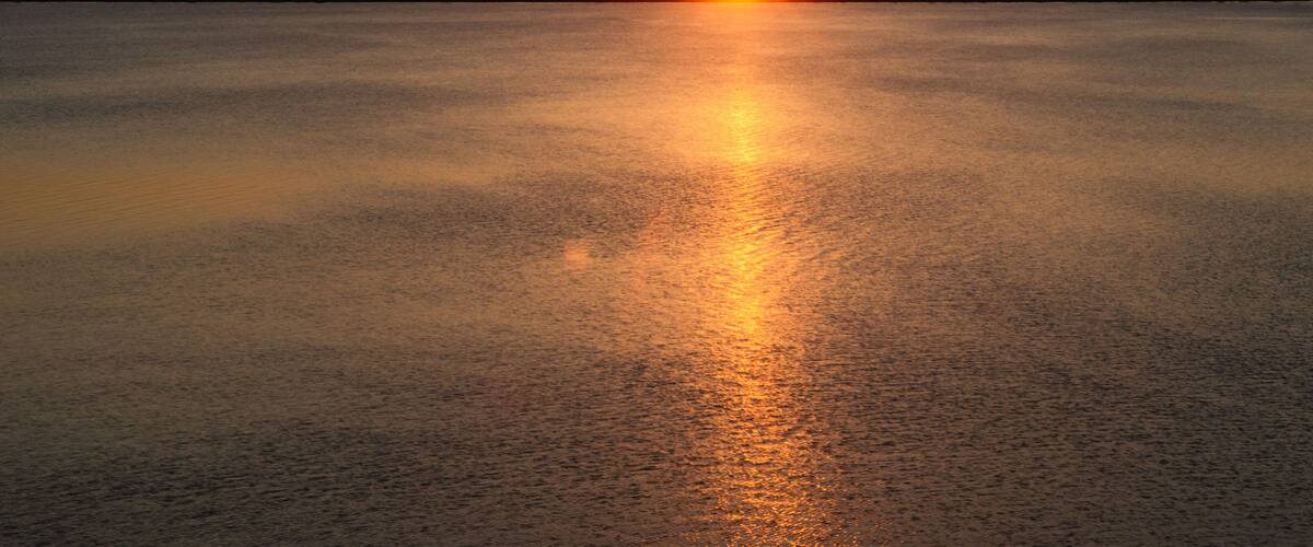 A sunset over a calm body of water with a silhouette of a hill in the background.