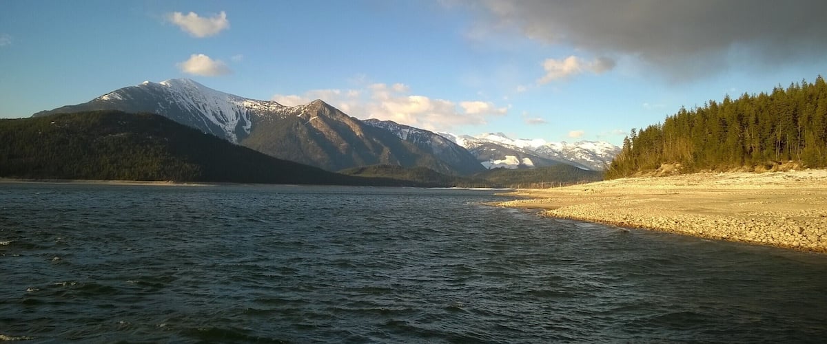 A lake with mountains in the background and a forest on the right.