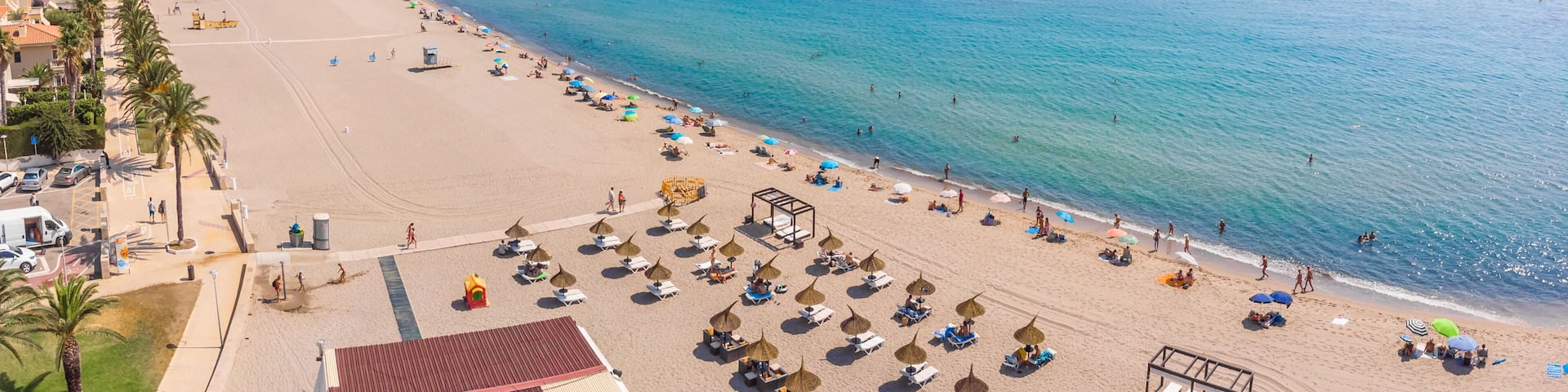 A beach with umbrellas, sun loungers, and a clear blue sea.
