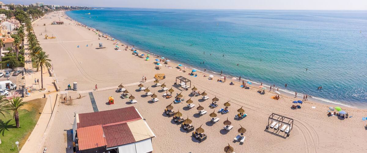 A beach with umbrellas, sun loungers, and a clear blue sea.