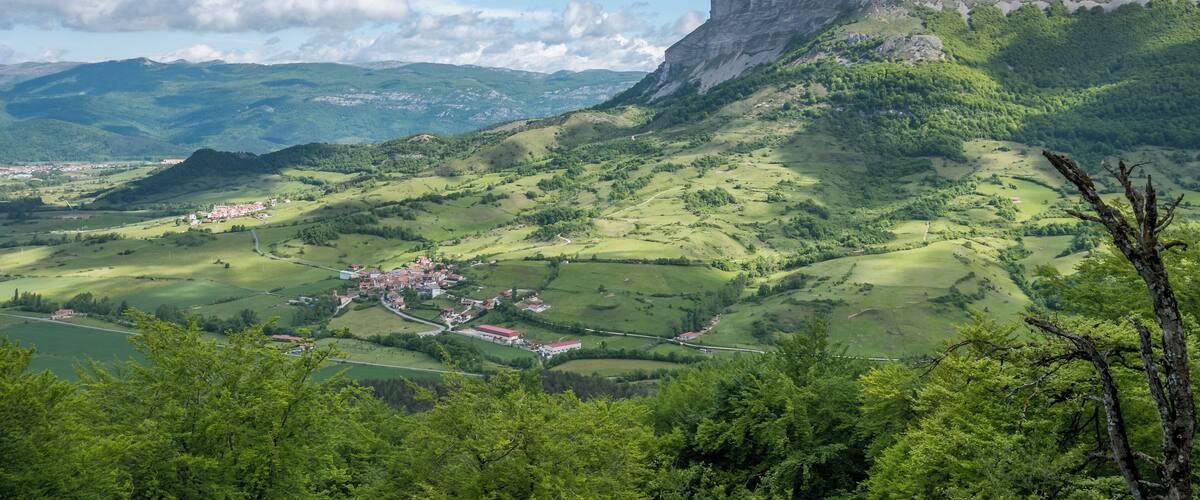 A mountainous landscape with a village nestled in the valley, surrounded by lush greenery and a prominent cliff.